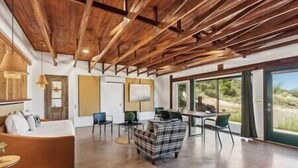 A spacious room with a wooden ceiling, a sofa, a plaid armchair, and a table with chairs.