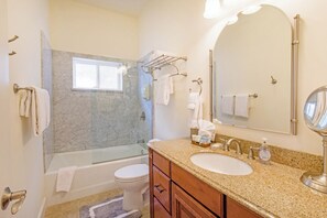 Un baño con bañera, inodoro, tocador con lavamanos y un espejo grande.