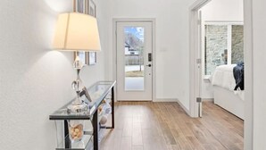 A hallway with a glass console table, a lamp, and a door leading to a bedroom with a stone wall and a bed. - World Cup Stay in Arlington – Walk to AT&T Stadium (Arlington)