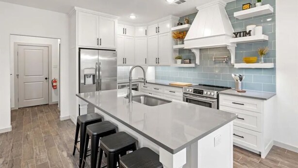 A modern kitchen with white cabinets, a stainless steel refrigerator, a large island with stools, and a backsplash with blue tiles. - World Cup Stay in Arlington – Walk to AT&T Stadium (Arlington)