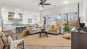 A modern living room with a sofa, coffee table, and chairs. There is a kitchen area with white cabinets and a dining table. - World Cup Stay in Arlington – Walk to AT&T Stadium (Arlington)