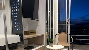 A modern hotel room with a bed, a small kitchenette, a TV, a balcony with a chair, and a view of the city at night. - Maravilloso loft con vista 707 (Bogotá)