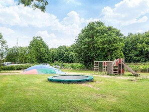 A playground with a trampoline, slide, and climbing structure in a grassy area with trees in the background. - 6 Person Holiday Park Home in Jelling (Jelling)