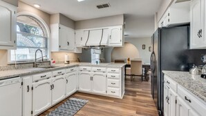 A modern kitchen with white cabinetry, a black refrigerator, and a window with blinds. - Farm House with an Amazing Pool in the desirable Western Hills in Temple TX (Temple)