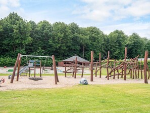 A playground with various play structures, including a slide and climbing frames, surrounded by a grassy area and trees. - 6 Person Holiday Park Home in Jelling (Jelling)