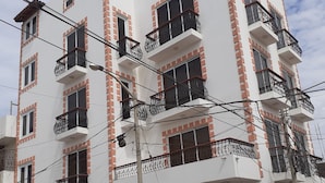 A multi-story building with balconies, a red car parked in front, and a three-wheeled vehicle. - Blanca Rosa's Place (Pacasmayo)