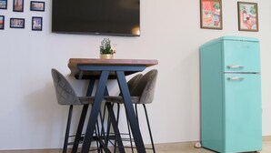 Ein modernes Wohnzimmer mit einem an der Wand befestigten Flachbildfernseher, einem türkisblauen Kühlschrank und einem kleinen Tisch mit zwei Barhocker.