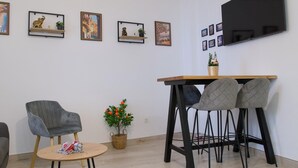 Ein modernes Wohnzimmer mit einem runden Holztisch, vier grauen Stühlen, einem grauen Sessel und einem kleinen Tisch mit verpackten Geschenken.