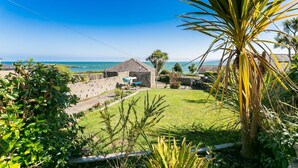 A coastal property with a stone building, a grassy lawn, and a view of the sea. - 7 Seaview - sleeps 4 guests  in 2 bedrooms (Moelfre)