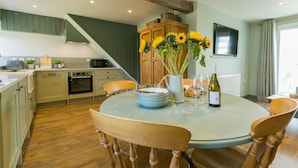 A dining area with a round table, chairs, a vase with sunflowers, wine glasses, and a bottle. - 7 Seaview - sleeps 4 guests  in 2 bedrooms (Moelfre)