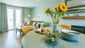 A dining area with a table set for four, a vase with sunflowers, and a bowl of salad. - 7 Seaview - sleeps 4 guests  in 2 bedrooms (Moelfre)