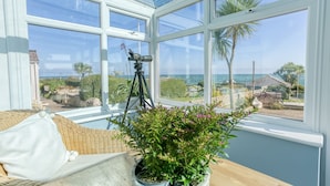 A conservatory with a telescope on a tripod, a wicker chair, and a potted plant. - 7 Seaview - sleeps 4 guests  in 2 bedrooms (Moelfre)