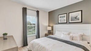 A bedroom with a bed, a nightstand, a lamp, a window with curtains, and two framed pictures on the wall.