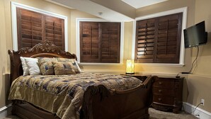 Une chambre à coucher avec un grand lit, une table de chevet, une commode et un téléviseur fixé au mur.