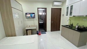 A compact kitchen with a dining area, a small desk, and a TV mounted on the wall.