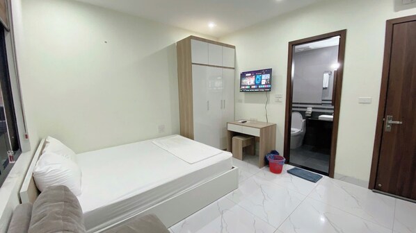A bedroom with a bed, a wardrobe, a desk, a television, and a bathroom visible through an open door. - Era Apartment Xuan Thuy (Hanoi)