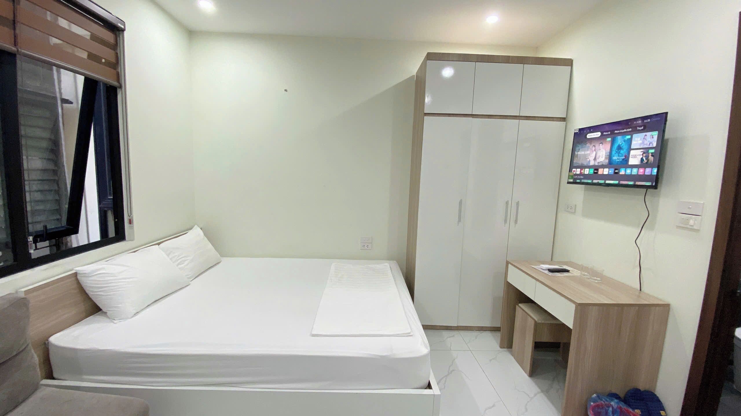 Quarto com cama, guarda-roupa, escrivaninha e televisão fixada na parede.