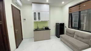 A compact kitchen with white cabinets, a black refrigerator, and a beige sofa near a window.
