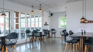 Ein moderner Essbereich mit schwarzen Stuhlgestellen aus Draht, Holzbeinen und Pendelleuchten. Große Fenster lassen natürliches Licht und Ausblicke nach außen herein.