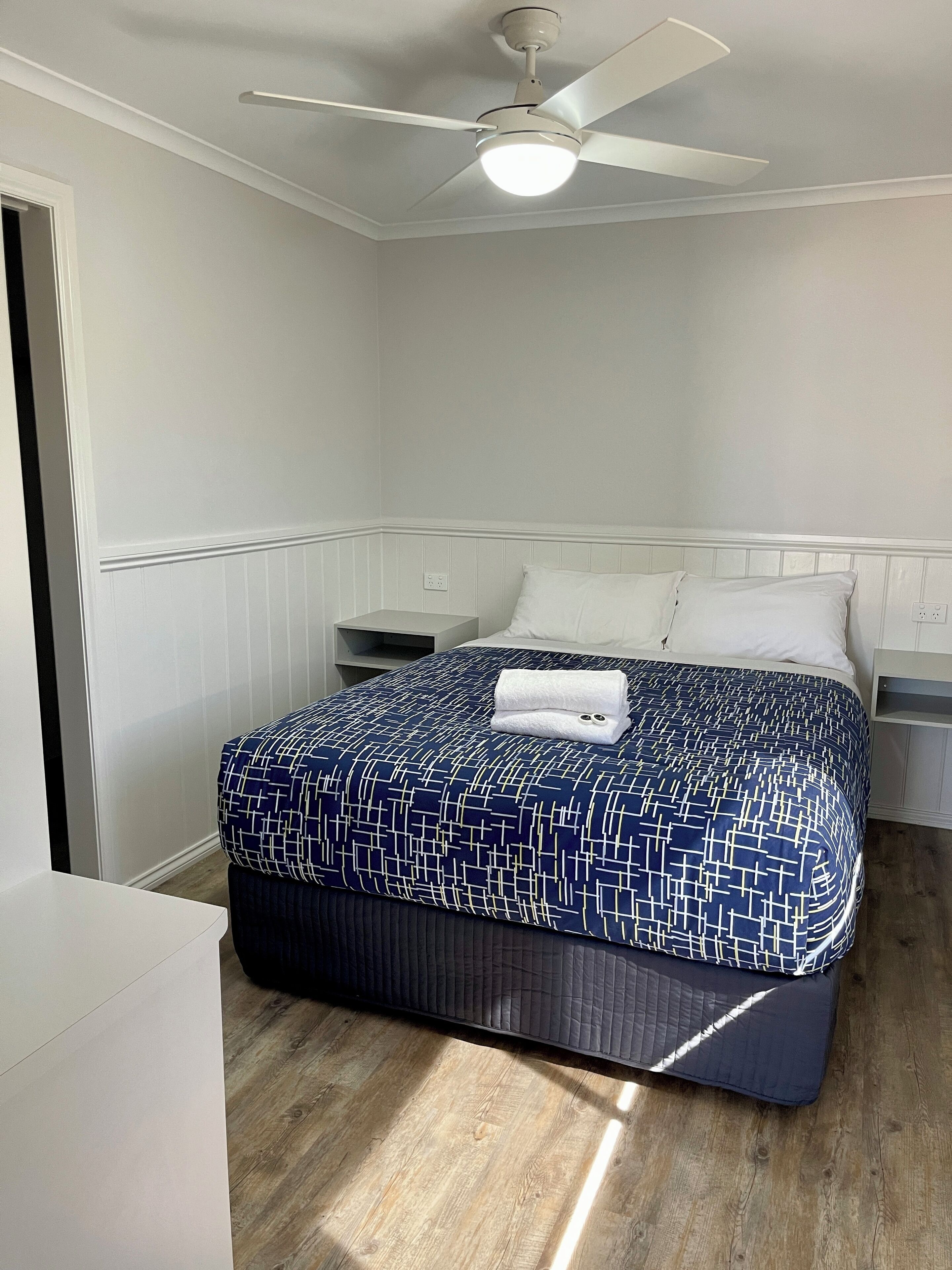 Un dormitorio ordenado con cama, mesita de noche y ventilador de techo.