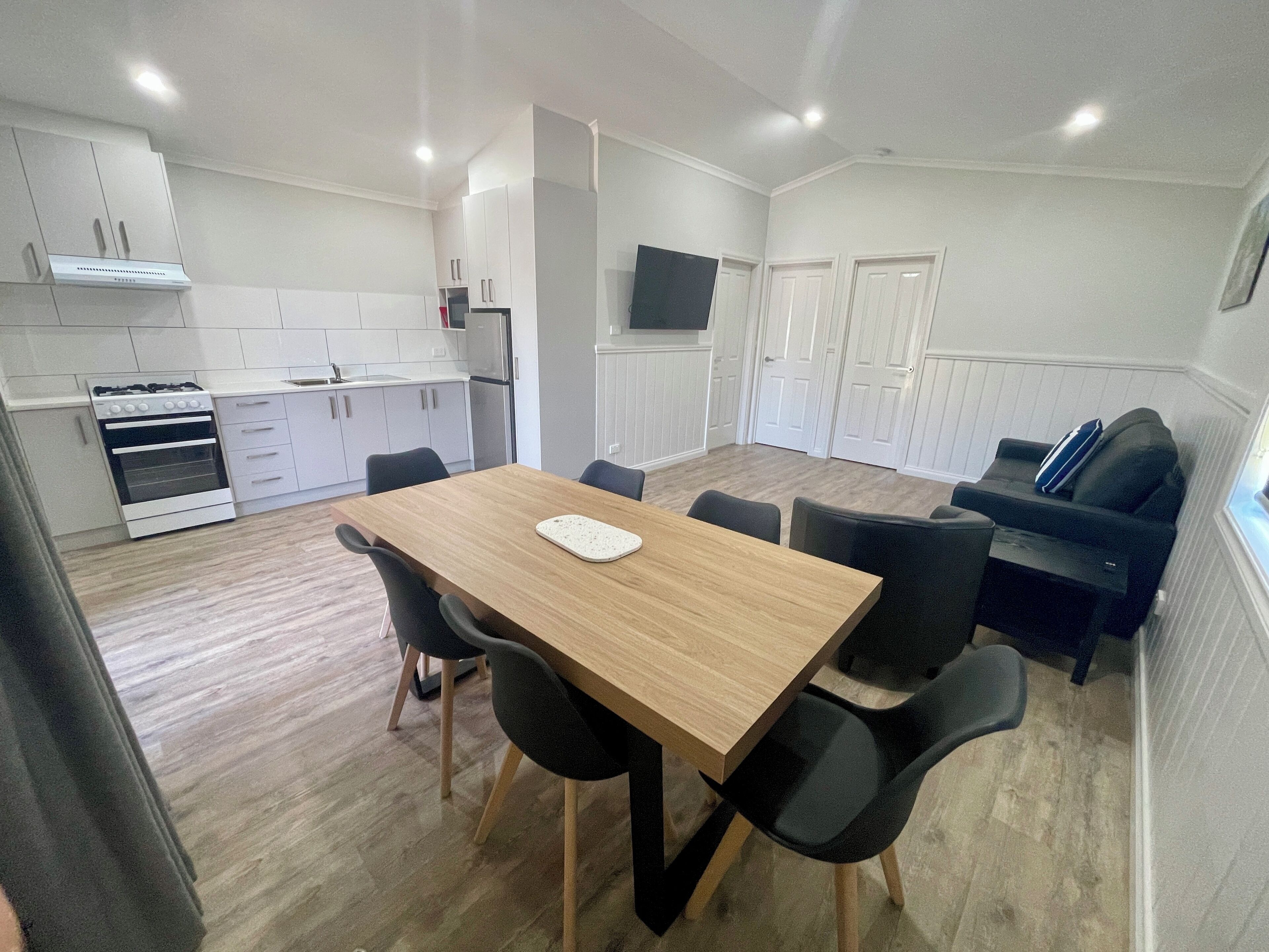 A modern kitchen with white cabinets, a built-in oven, and a dining area with a wooden table and black chairs.