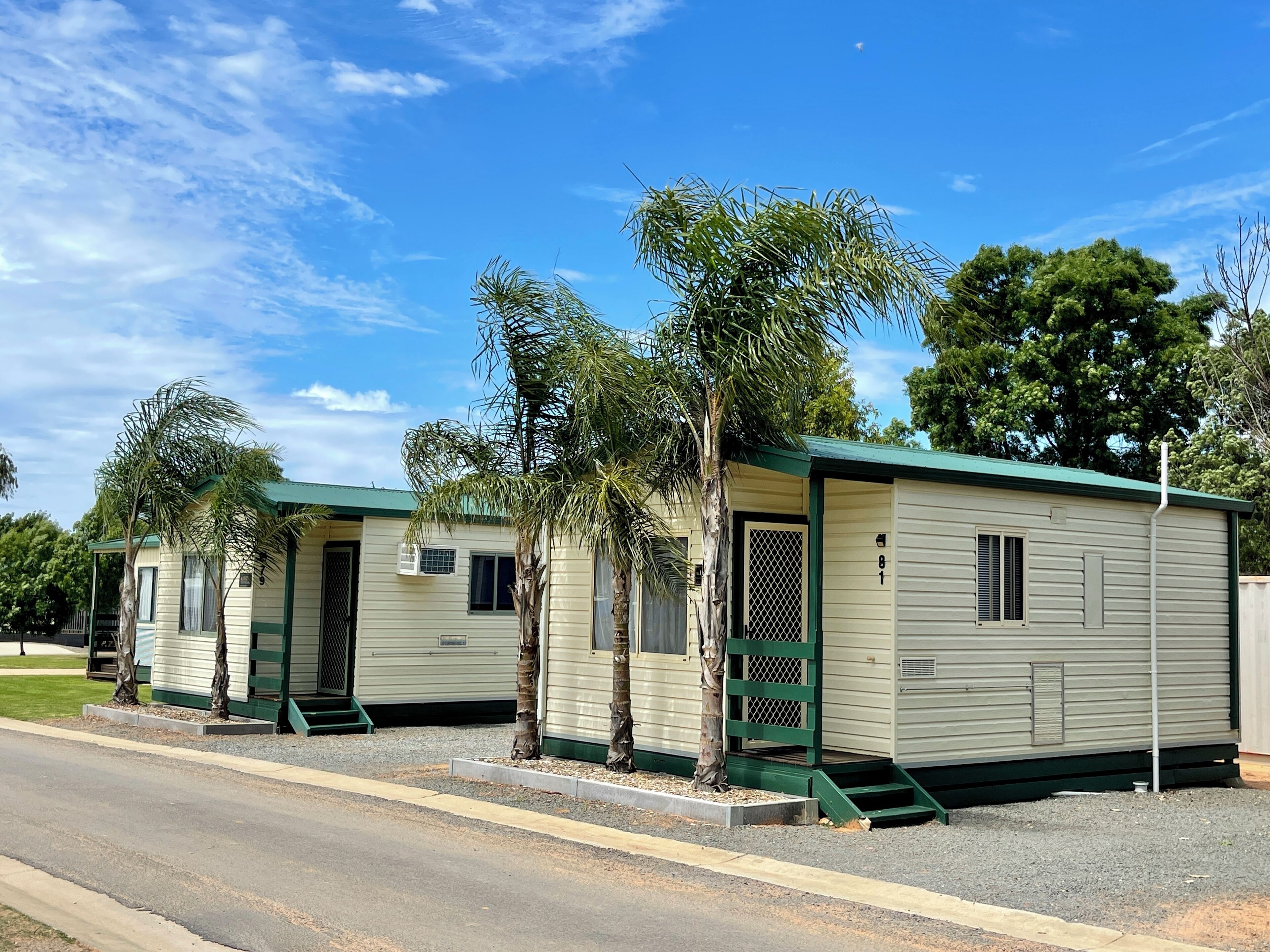 A row of mobile homes with green trim and a covered porch area, each with a small window and a door.