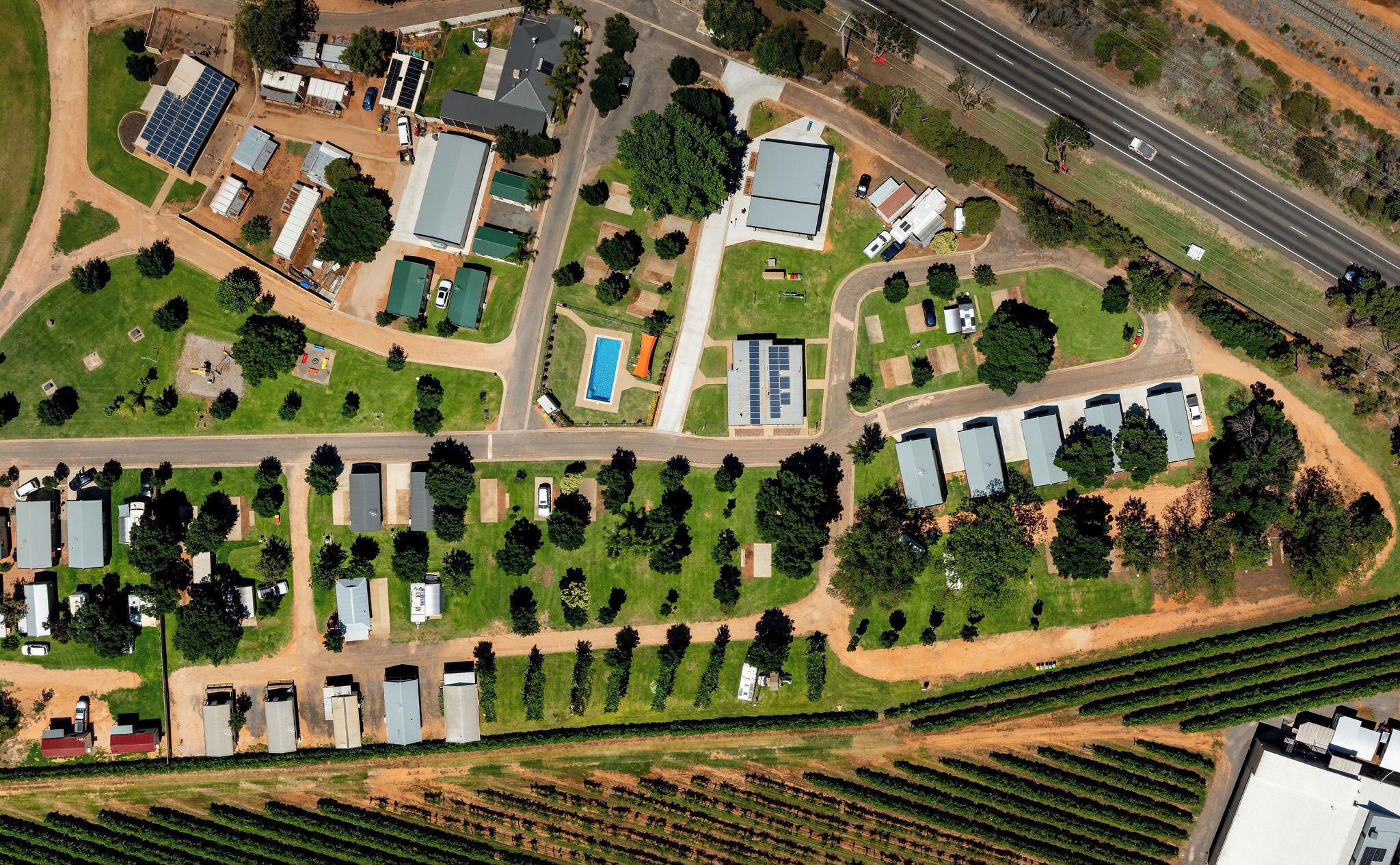 An aerial view of a residential area with multiple detached houses, a swimming pool, and a large building with solar panels.