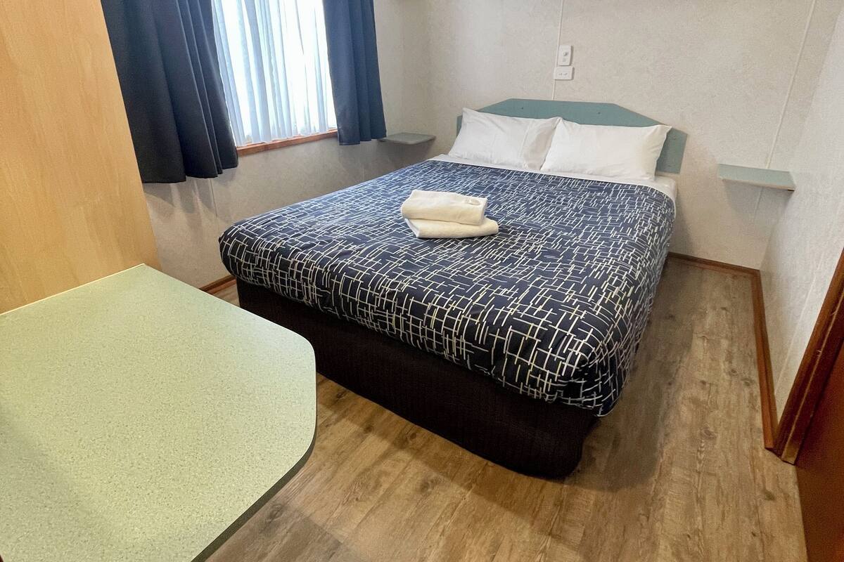 Une chambre avec un lit, un bureau, un ventilateur de plafond et une fenêtre avec des rideaux.