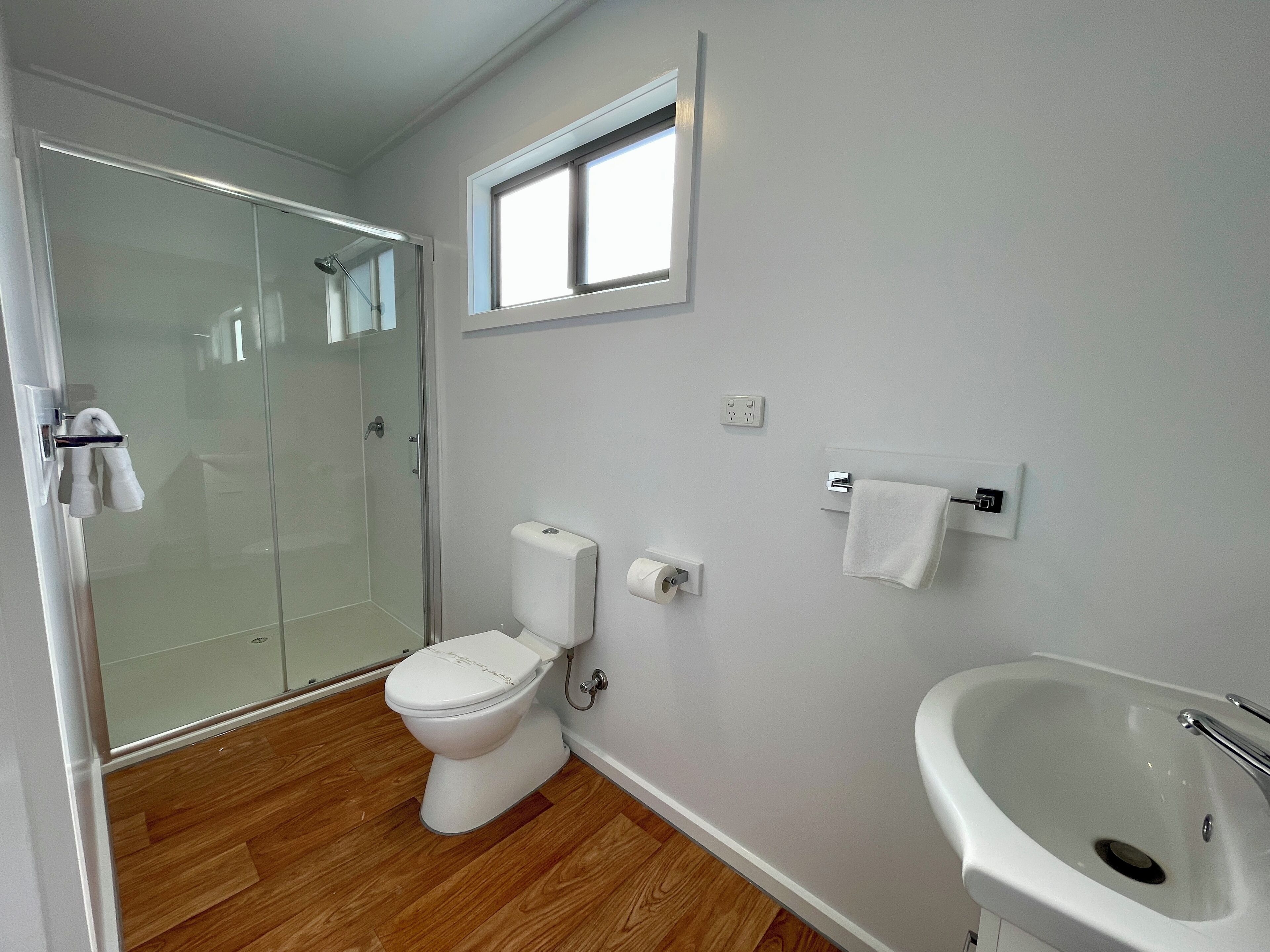 A bathroom with a toilet, a sink, a shower, and a window.
