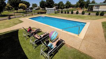 Une piscine rectangulaire dont les bords sont recouverts de carreaux, entourée d’une pelouse bien entretenue et d’une clôture en métal.