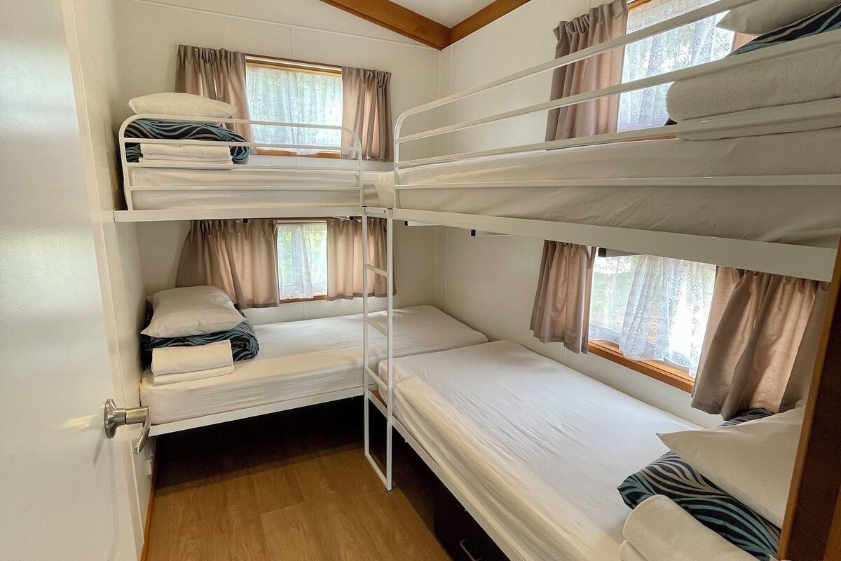 Une chambre avec trois lits superposés, des poutres en bois et des fenêtres avec des rideaux.