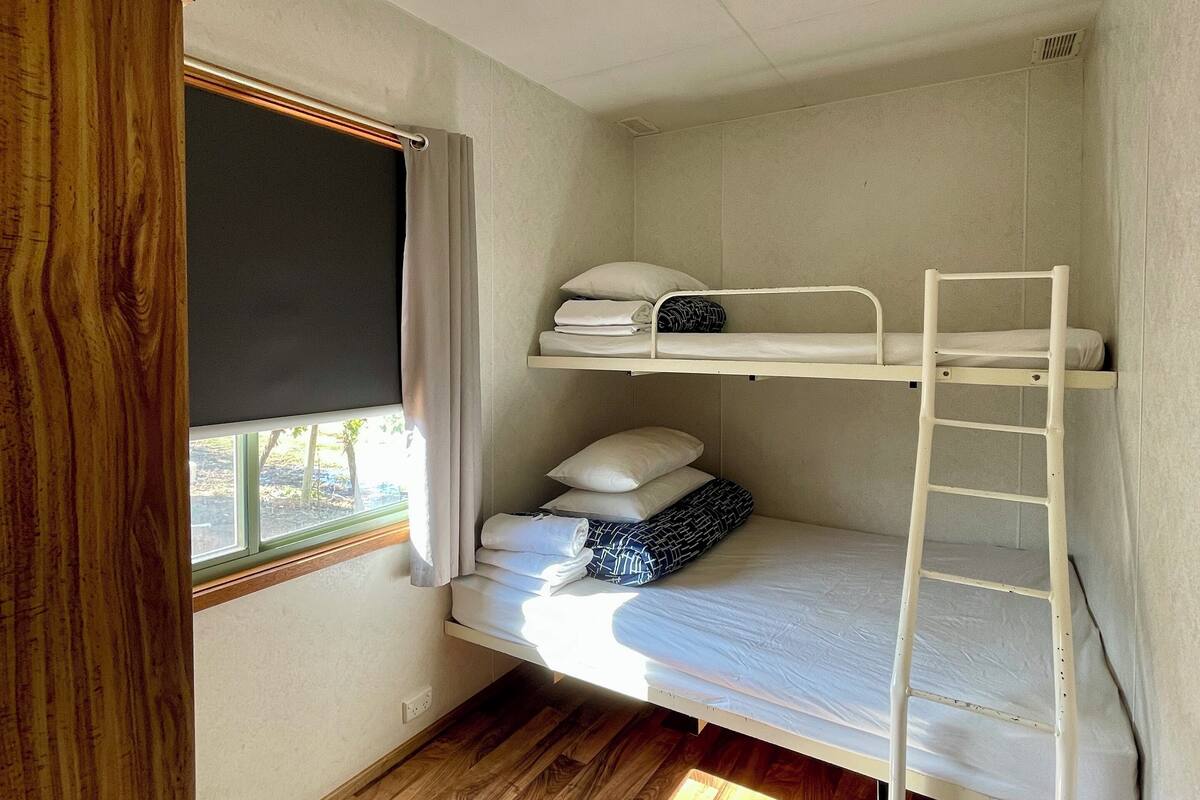Une chambre avec un lit superposé, une fenêtre, un plancher en bois et un luminaire au plafond.
