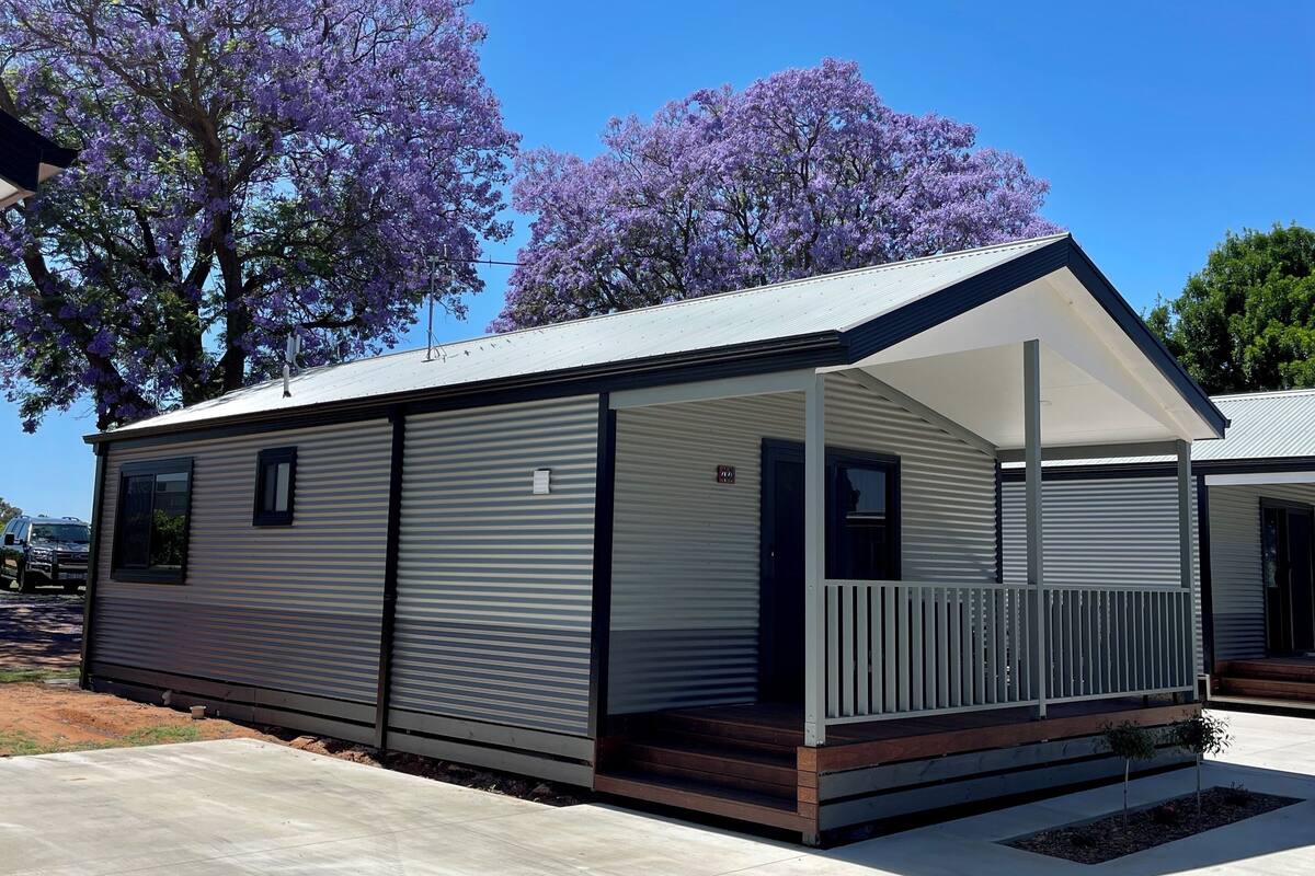 Une maison mobile moderne dotée d’un porche couvert, de grandes fenêtres et d’un toit plat.