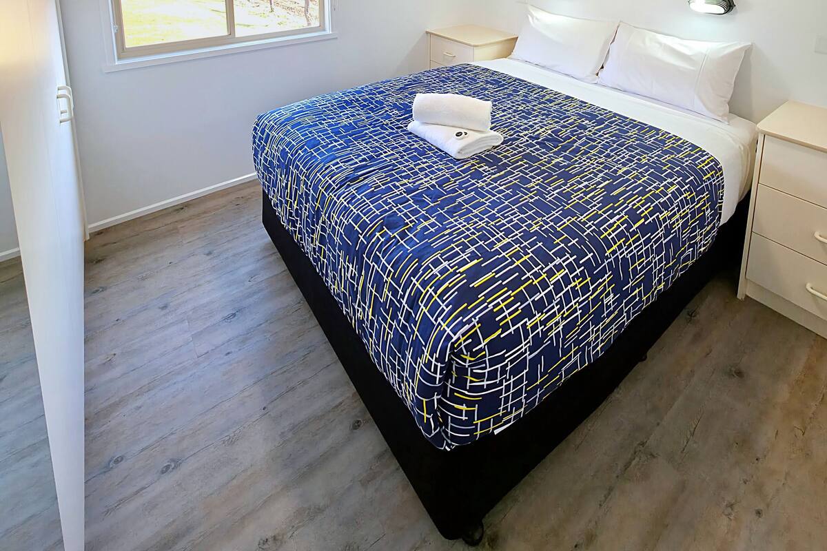 Une chambre à coucher avec un lit, un ventilateur de plafond, une fenêtre donnant sur un beau paysage et une table de chevet.