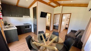 A compact kitchen with modern appliances, a dining area with a glass table and chairs, and a living area with a sofa and curtains. - BIG4 Red Cliffs Holiday Park (Red Cliffs)