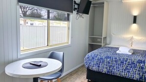 A bedroom with a bed, a TV mounted on the wall, a small table with a chair, and a window with blinds. - BIG4 Red Cliffs Holiday Park (Red Cliffs)