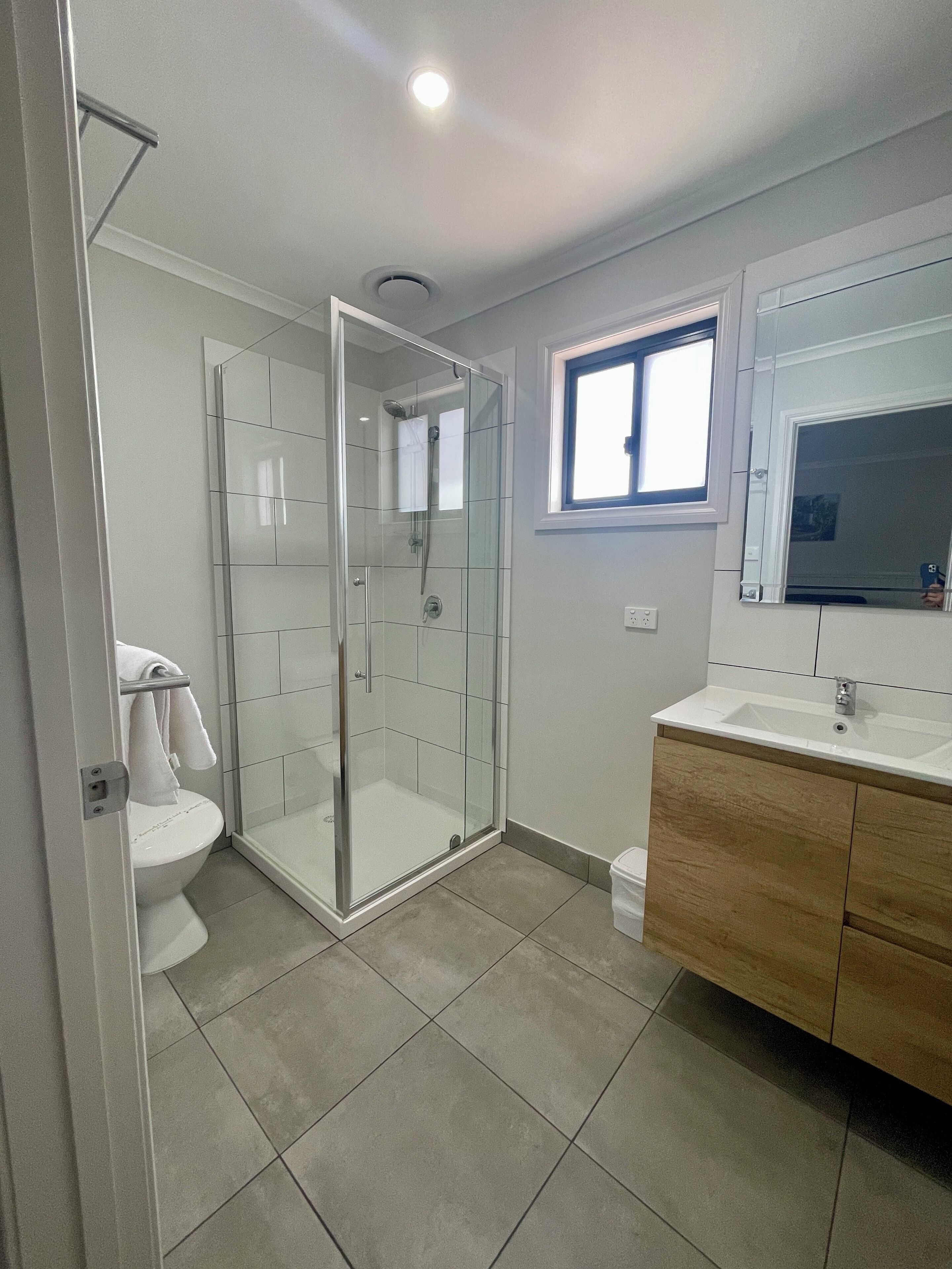 A modern bathroom with a glass-enclosed shower, a white toilet, and a wooden vanity with a sink.