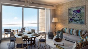 Ein modernes Wohnzimmer mit großem Fenster, einem Essbereich mit rundem Tisch und einer Couch mit gemusterten Kissen.