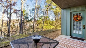 A covered outdoor seating area with a table and chairs, a door with a wreath, and a view of a forested area. - Monarch of the Mountain pool (Pigeon Forge)