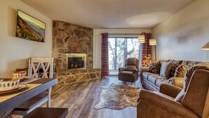 A cozy living room with a stone fireplace, a sofa, a chair, and a dining table with bowls. - Monarch of the Mountain pool (Pigeon Forge)