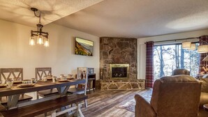 A cozy living room with a stone fireplace, wooden furniture, and a large window with curtains. - Monarch of the Mountain pool (Pigeon Forge)