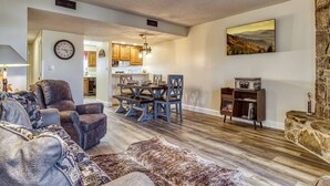A spacious living room with a large sofa, a dining area with a wooden table and chairs, and a kitchen in the background. - Monarch of the Mountain pool (Pigeon Forge)