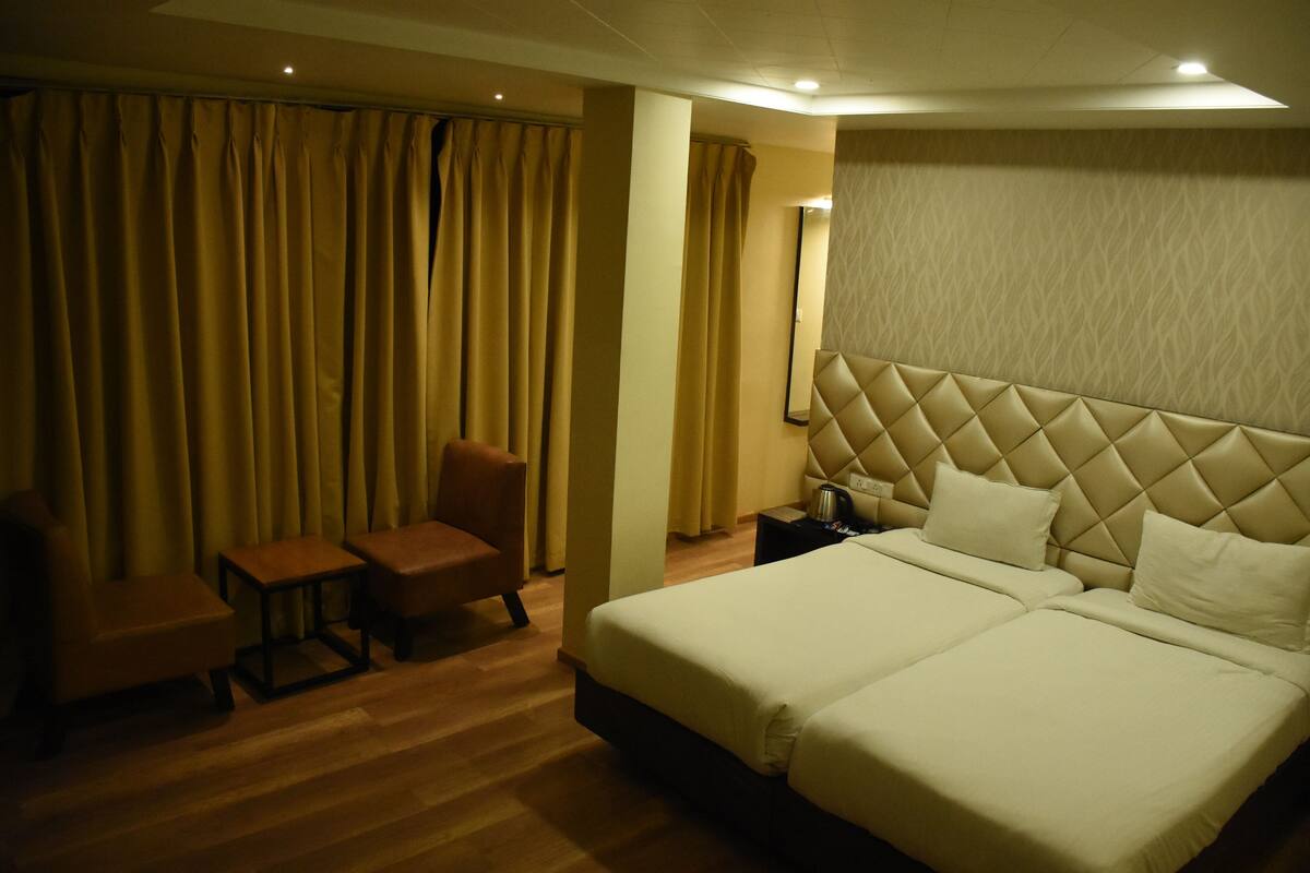 A hotel room with two beds, a chair, a small table, and a mirror.
