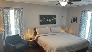 Ein Schlafzimmer mit einem Bett, einem Sessel, einem Deckenventilator und einem Bild an der Wand.