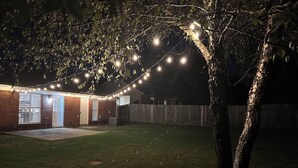 Ein Garten mit einem Ziegelhaus, einem Holzzaun und Lichterketten.