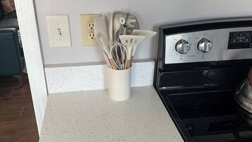 Une cuisine dotée d’un plan de travail blanc à motifs, d’une cuisinière en acier inoxydable et d’un porte-ustensiles blanc contenant divers outils de cuisine.