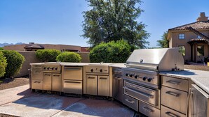 Een buitenkeuken van roestvrij staal met een grill, meerdere branders en opbergladen.