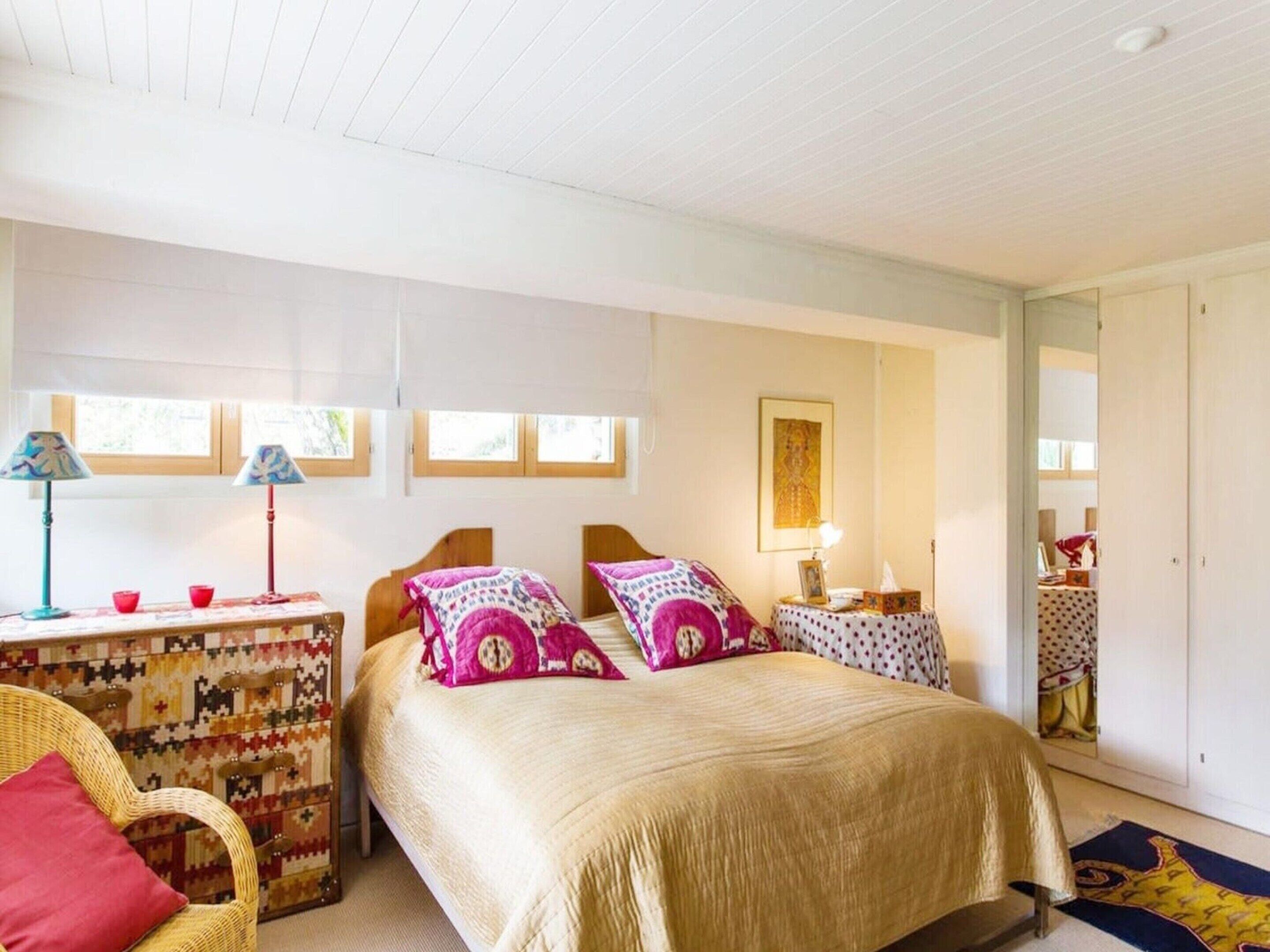 A bedroom with a bed, two bedside tables, a chair, a window, and a door.