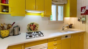 Una cucina con mobili gialli, un piano di lavoro bianco, un fornello a gas e una finestra che si affaccia sul verde.