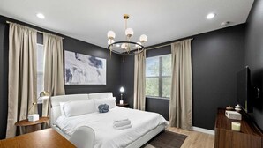A modern bedroom with a large bed, a chandelier, and a flat-screen TV.